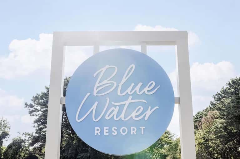 Blue Water Resort entrance sign with white frame against cloudy sky and green trees