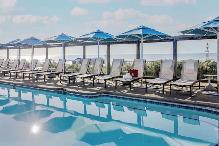 Resort pool deck with blue umbrellas, lounge chairs, and panoramic ocean horizon view