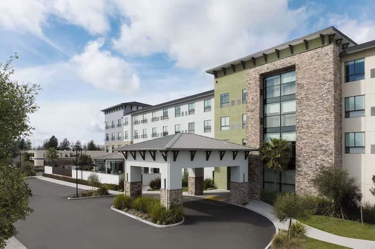 Hotel exterior entrance with modern architecture, mixed stone and brick facade, covered porte-cochere, and landscaping