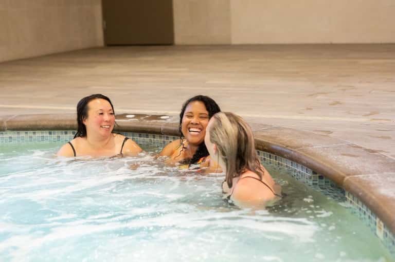 Three women relaxing and smiling in indoor hot tub with wooden surround