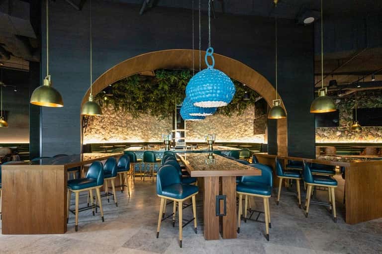 Contemporary restaurant with blue textured pendant light, wooden tables, blue chairs, and decorative wall