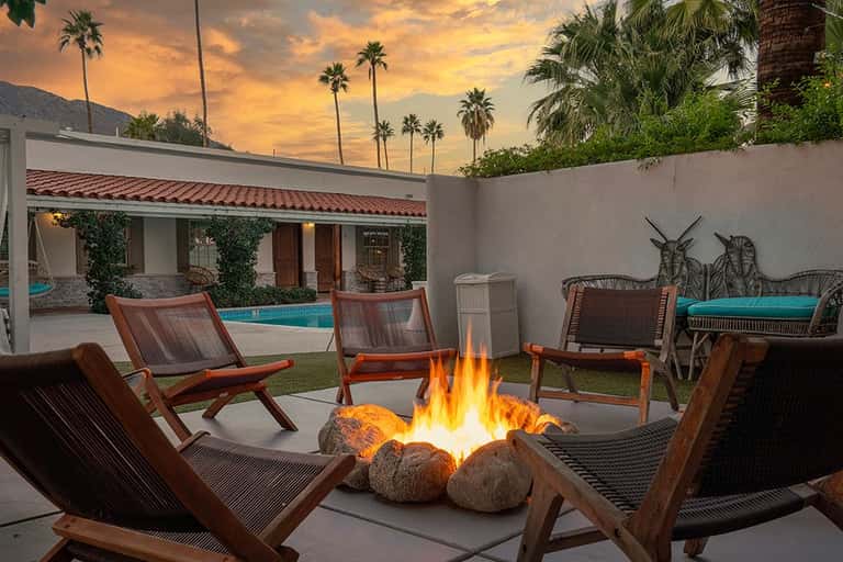 Fire pit area with mid-century modern wooden chairs overlooking a resort pool at dusk with palm trees