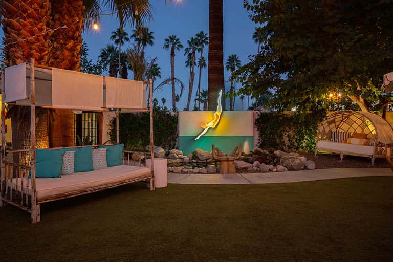Nighttime resort courtyard with cushioned lounges, colorful wall art, and palm trees under blue sky