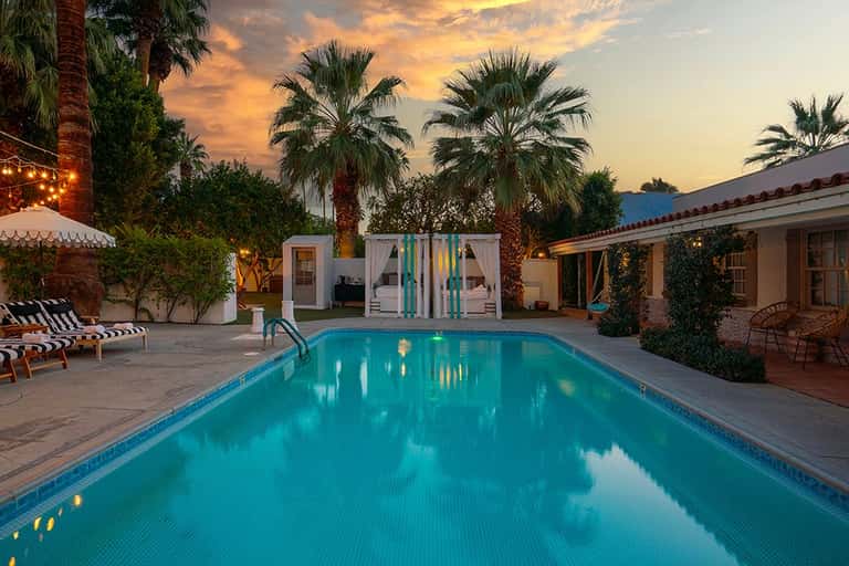 Resort pool at sunset with spa cabanas, ivy-covered walls, and palm tree-lined grounds