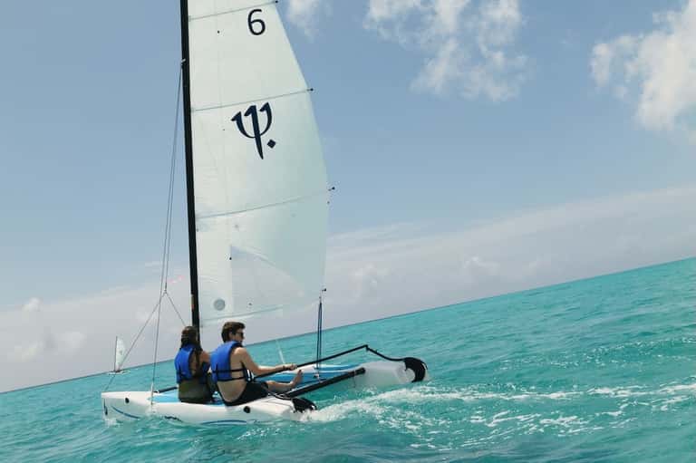 Two people sailing a small white sailboat on turquoise tropical water