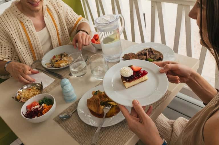 Two women dining together at a bright seaside restaurant with various plated dishes and water pitcher