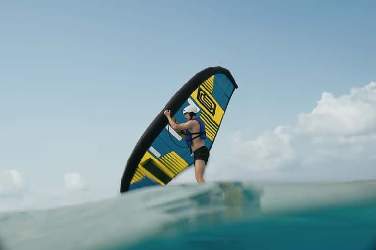Kitesurfer in mid-air performing tricks on bright turquoise water under clear blue sky