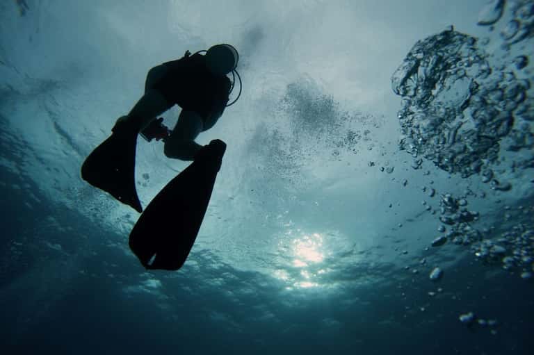 Scuba diver in silhouette exploring underwater coral reef with light filtering from surface above