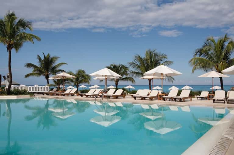 Infinity pool with white umbrellas and lounge chairs overlooking calm turquoise ocean and palm trees