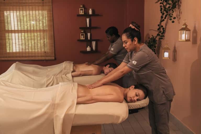 Spa massage room with therapists providing relaxation treatment to two clients on massage beds
