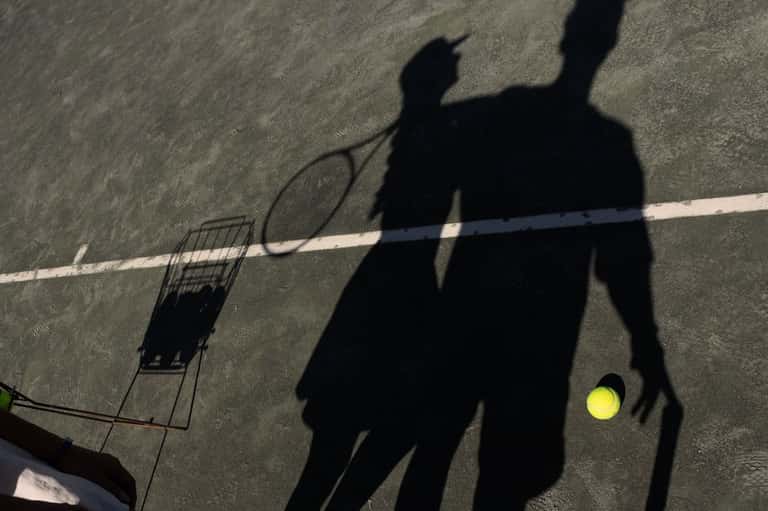 Shadow of person playing tennis with yellow ball on outdoor court
