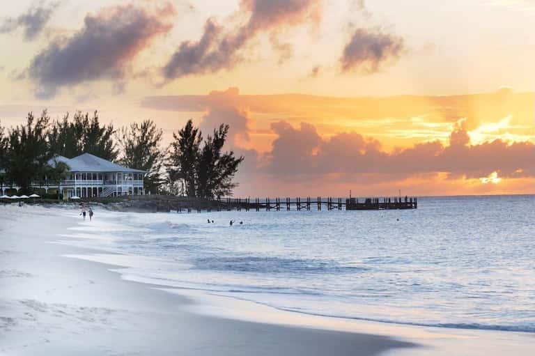 Beachfront sunset with white building, pier, and waves crashing on sandy shore