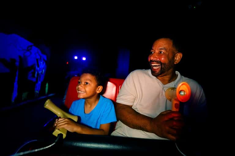 Father and son smiling while playing laser tag in dark arena with neon lights