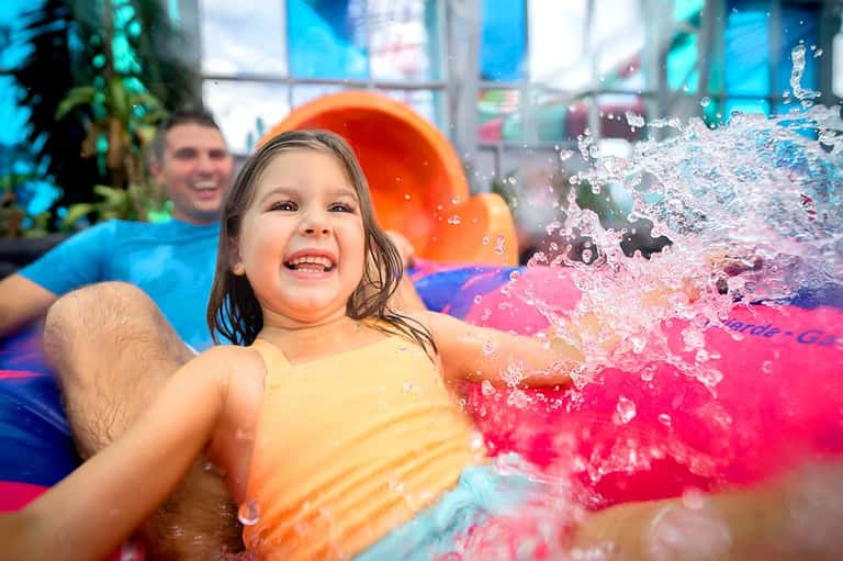 Young girl splashing in colorful wave pool with man watching in background