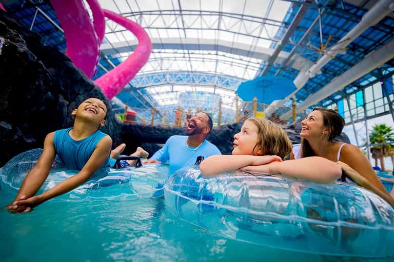 Family of four relaxing in indoor tropical wave pool with colorful decorations overhead