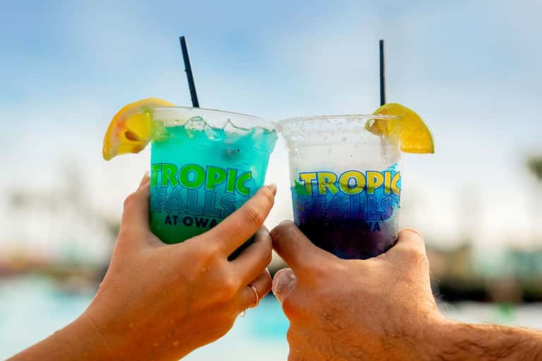 Tropical cocktails with blue and purple layered drinks, lemon slices, and straws