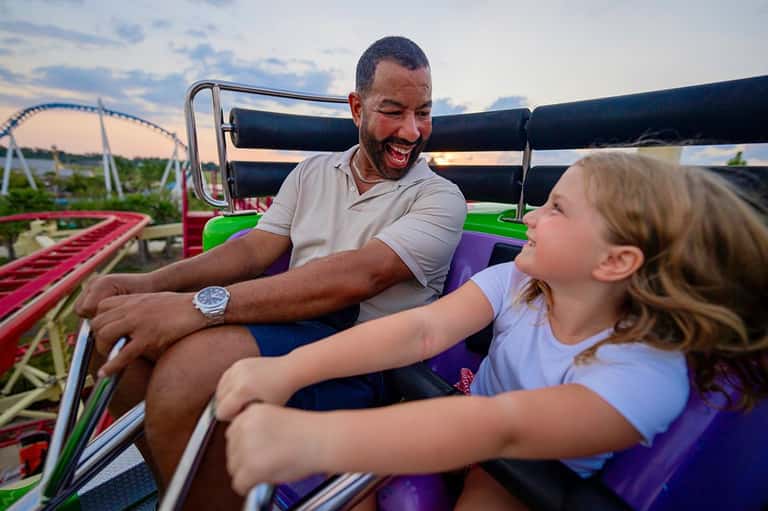 Father and daughter laughing together on a colorful roller coaster car at an amusement park