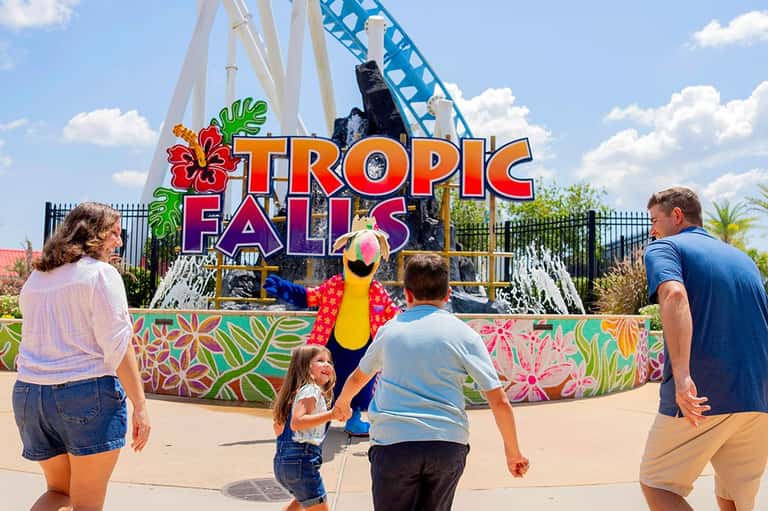 Family posing with a costumed tropical bird character at Tropic Falls theme park entrance sign
