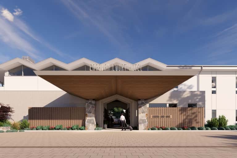 Caravan Court Hotel exterior with distinctive curved wooden canopy entrance, white brick facade, and manicured landscaping