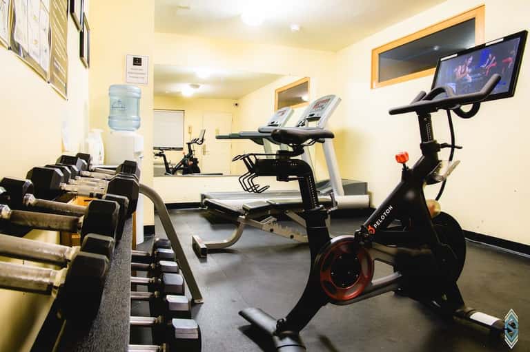 Fitness center with exercise bikes, dumbbells, treadmill, and wall-mounted screens