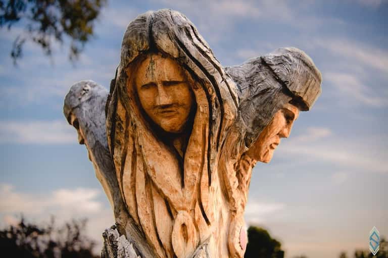 Wooden carved sculpture of three faces outdoors against cloudy sky