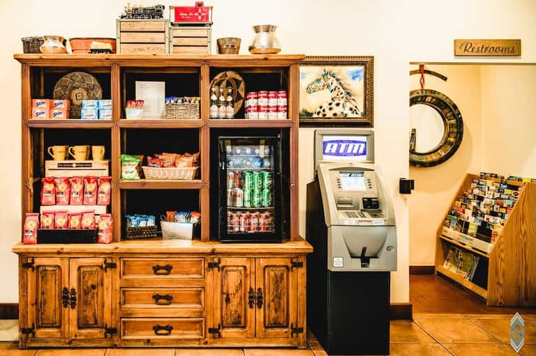 Rustic wooden display cabinet with shelves holding snacks, beverages, ATM, and decorative train models with horse artwork