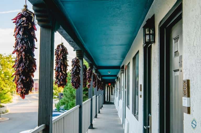 Covered balcony or corridor with turquoise ceiling, decorative red chili pepper ristras hanging, and white railings