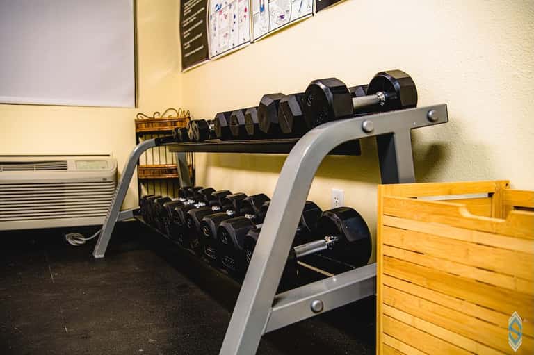 Exercise room displaying rack of dumbbells in various weights on gray metal stand with weight bench visible