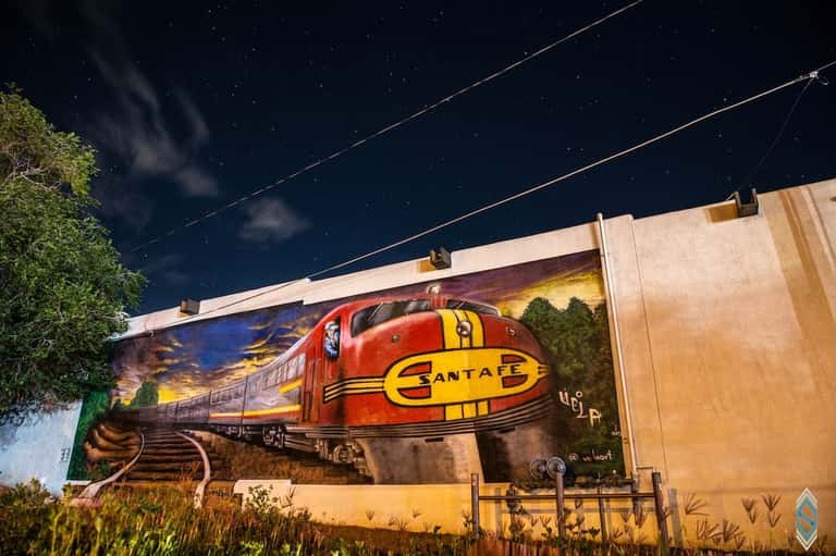 Vintage Santa Fe passenger train mural painted on building exterior against evening sky with power lines