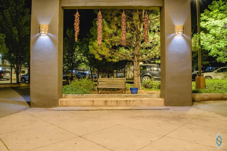 Illuminated covered pavilion with concrete bench and landscaped trees at night in resort courtyard