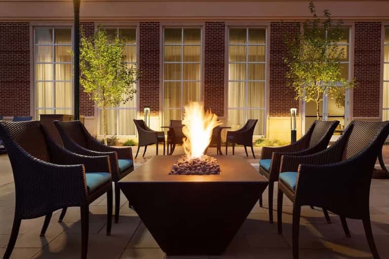 Outdoor fire pit lounge at night with wicker chairs and brick building backdrop