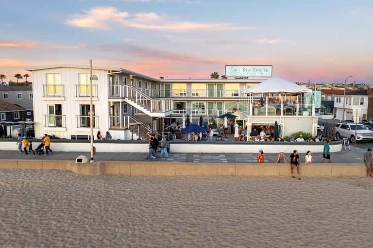 Sea Sprite beach club exterior at dusk with modern architecture, outdoor seating, and beachgoers on sandy shore