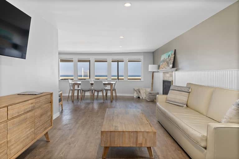 Contemporary suite living space with ocean-view windows, fireplace, wooden furniture, and cream-colored seating