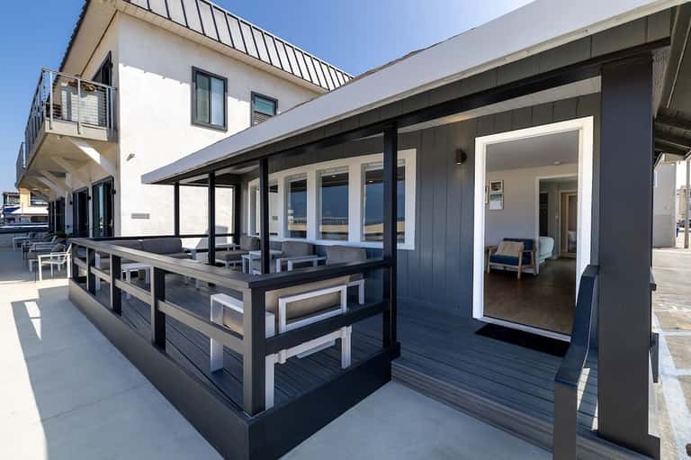 Modern oceanfront deck with black and white railings, covered patio, and glass doors to interior spaces