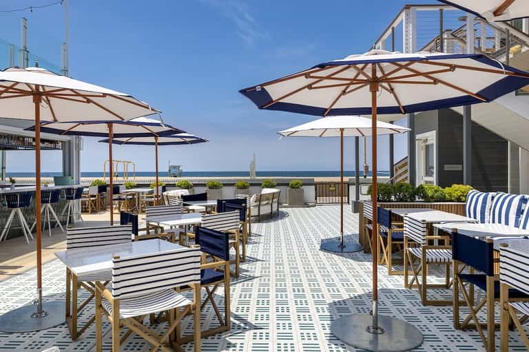 Expansive oceanfront patio with umbrella-shaded tables, striped seating, and panoramic water views
