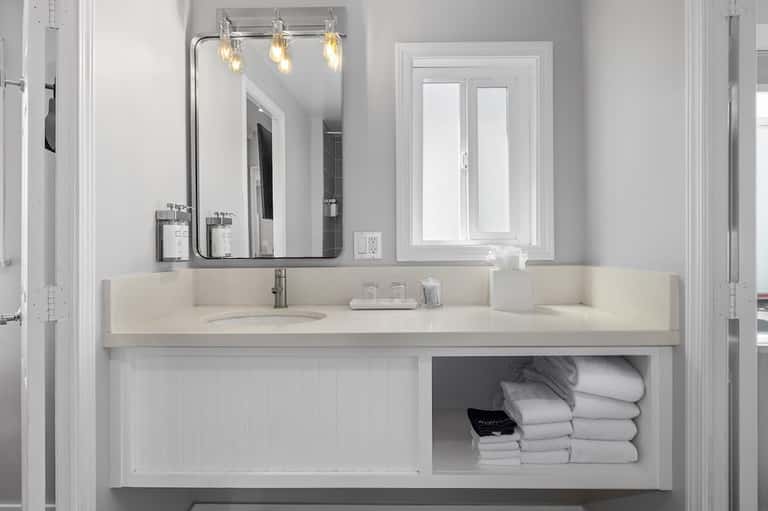 Modern white bathroom with long vanity, pendant lights, large mirror, and shelving with towels