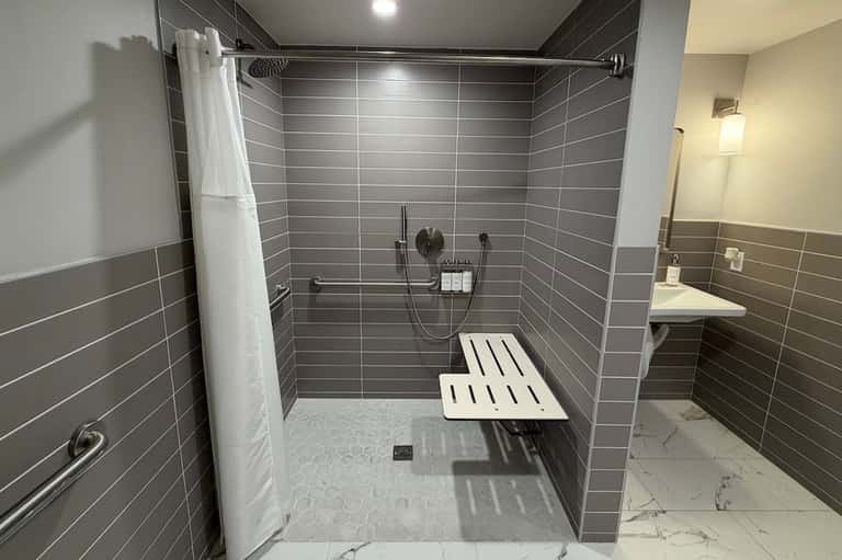Spacious walk-in shower with gray horizontal tile, white bench seating, and rainfall showerhead