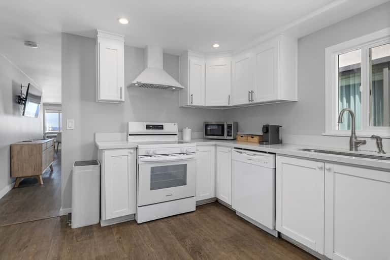 Modern white kitchen with stainless steel appliances, quartz countertops, and wood flooring