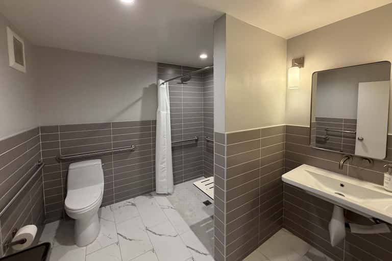 Bathroom with gray tile walls, white sink vanity, toilet, and large mirror