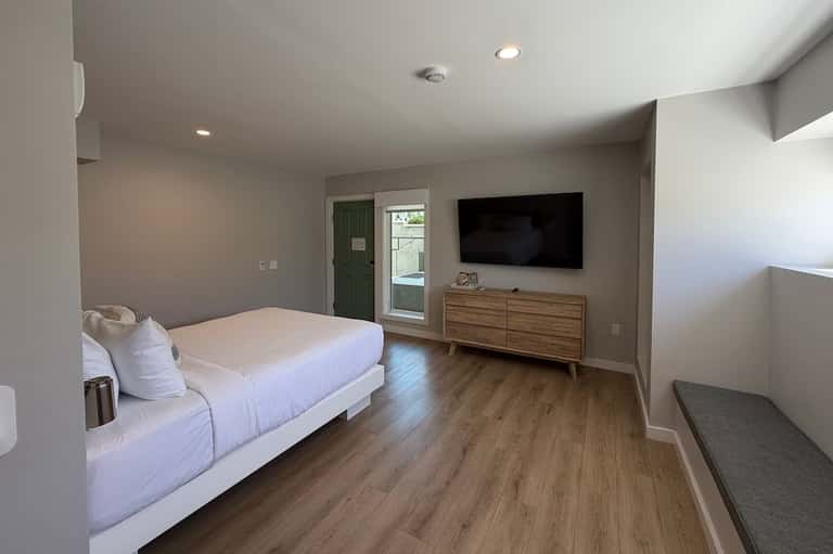 Modern bedroom suite with queen bed, wooden dresser, TV, patio doors, and lounge area