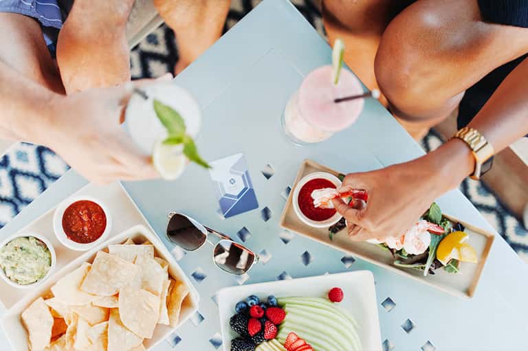 Overhead view of poolside dining with fresh fruit, appetizers, and cocktails