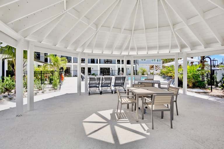 Covered outdoor pavilion with dining table, lounge chairs, and coastal landscape view