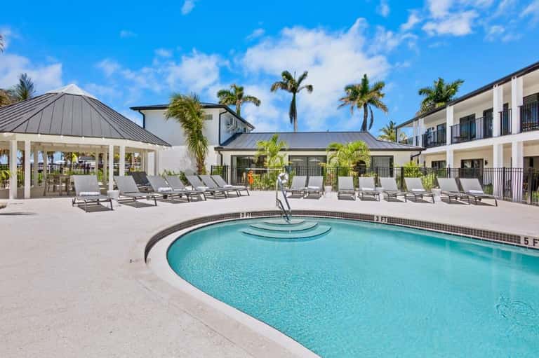 Resort pool courtyard with lounge chairs, cabana, palm trees, and modern white architecture