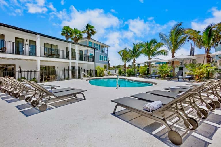 Modern apartment building with curved pool, lounge chairs, and white umbrellas in sunny courtyard