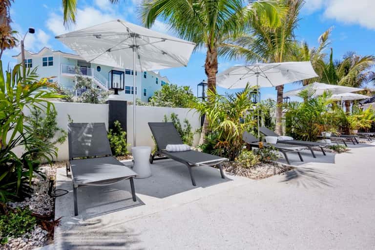 Shaded lounge area with gray chairs, white umbrellas, and tropical plants near beachfront