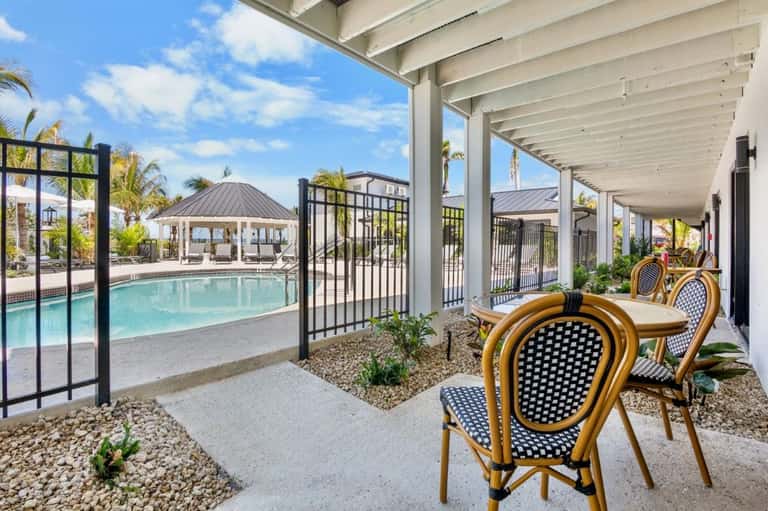 Covered patio with dining chairs, pool view, and black railings in bright daylight