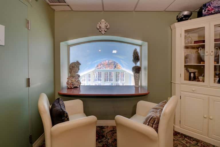 Cozy media room with two cream chairs facing a window displaying the indoor pool facility