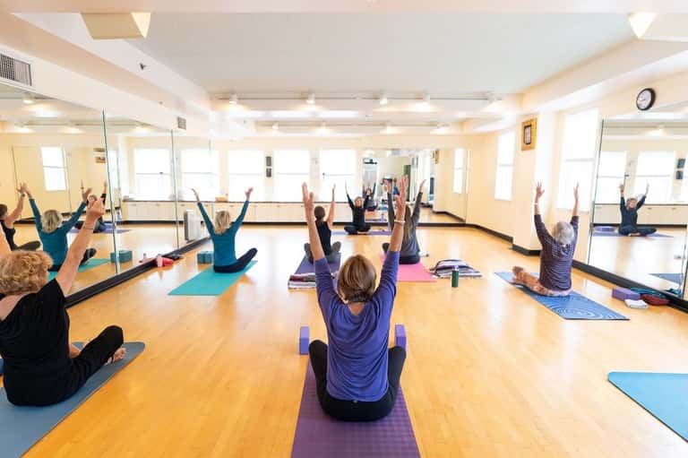Yoga class with participants on mats in a bright studio with mirrors and natural light