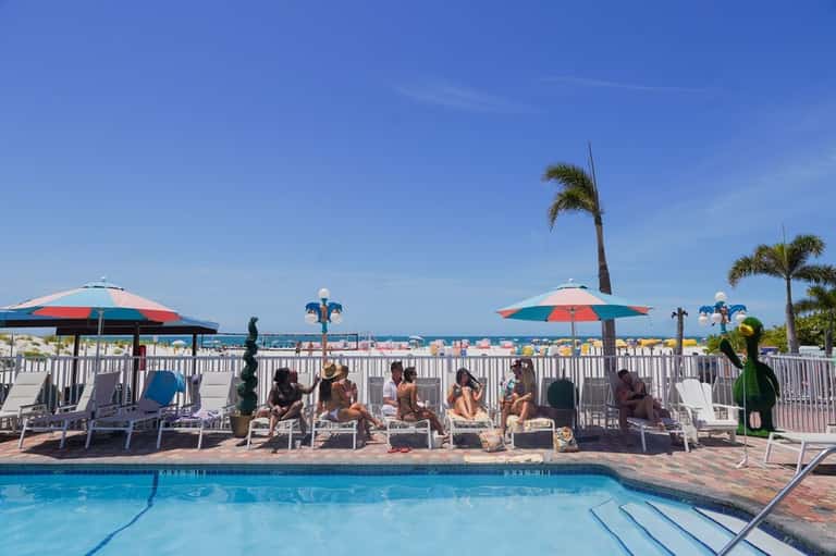 Resort pool with clear blue water, white railings, lounge chairs with umbrellas, and ocean view beyond