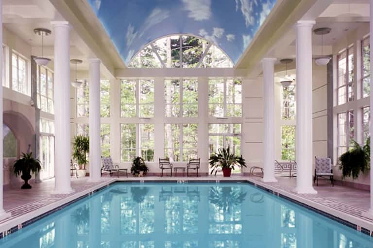 Elegant indoor pool surrounded by tall windows and classical columns with natural light